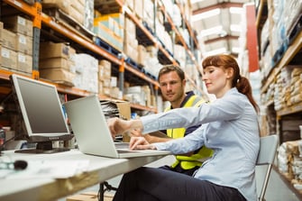 Warehouse worker and manager looking at laptop in a large warehouse